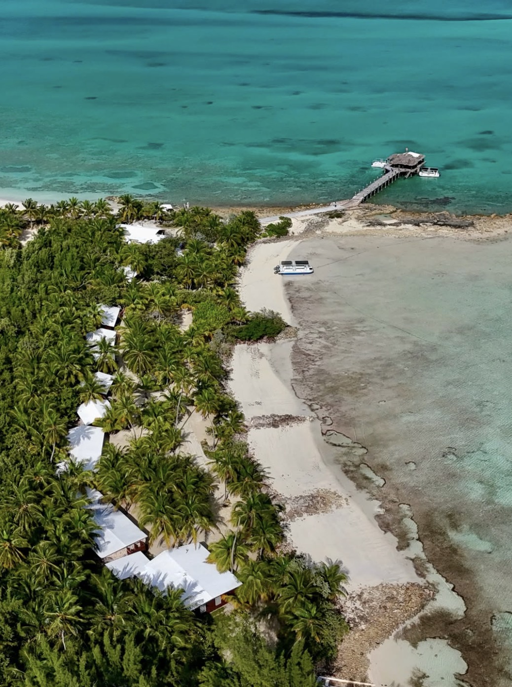 Aerial view of Small Hope Bay Lodge cottages and pier in turquoise Andros water.